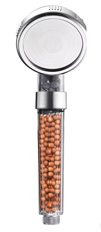 Handheld chrome shower head with a transparent filter cartridge showing brown mineral beads inside.